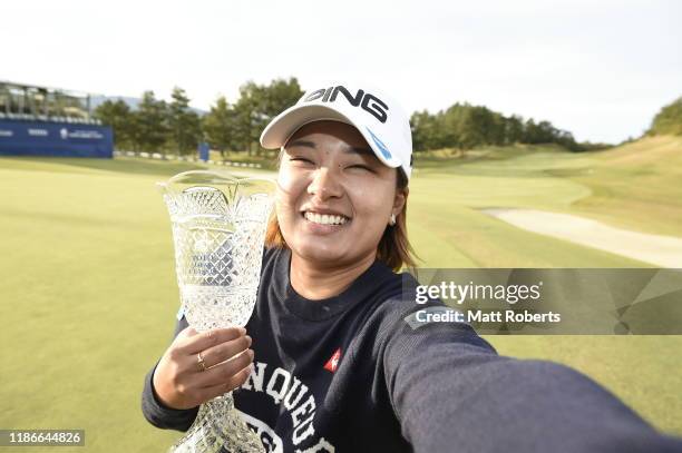 Ai Suzuki of Japan pretends to take a selfie while holding the trophy on the 18th green after winning the final round of the TOTO Japan Classic at...