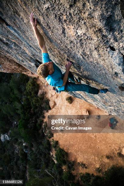 climber sticks a hold while high off the ground - soloklettern stock-fotos und bilder