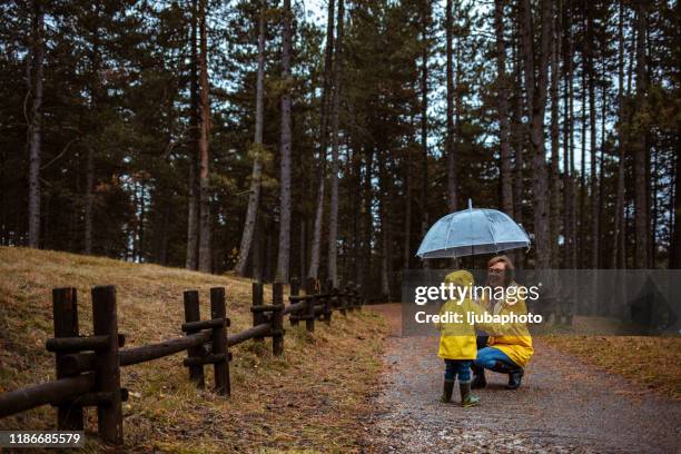 mutter und sohn in regenmänteln unter regenschirm im regen - mother protecting from rain stock-fotos und bilder