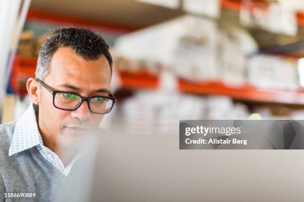 manager checking stock on a computer in a busy small warehouse - distribution warehouse technology stock pictures, royalty-free photos & images