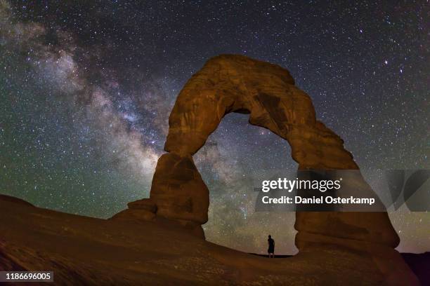 delicate arch, arches national park, utah at night with person watching milky way - arches national park stockfoto's en -beelden