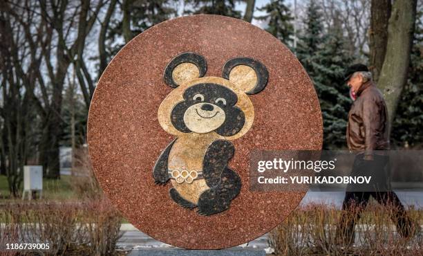 Man walks behind a monument to the mascot for the 1980 Moscow Olympics - Misha the bear - near the Luzhniki stadium in Moscow on December 6, 2019. -...