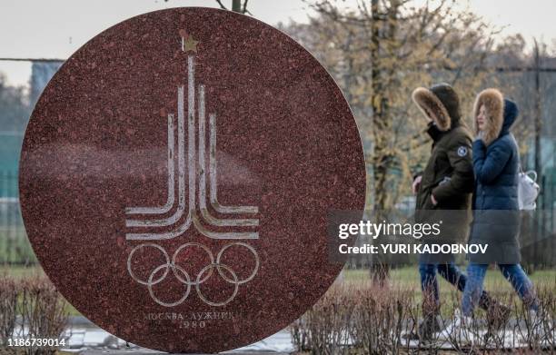 Couple walks behind a monument featuring the emblem of the 1980 Moscow Olympics near the Luzhniki stadium in Moscow on December 6, 2019. - The...