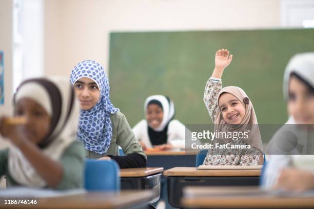 muslim student raises her hand for a question stock photo - islam stock pictures, royalty-free photos & images
