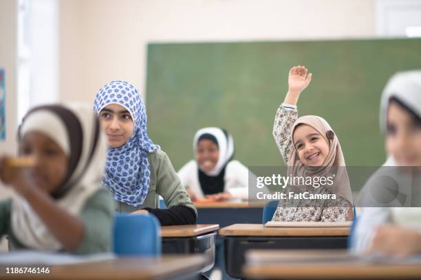 muslim student raises her hand for a question stock photo - islam imagens e fotografias de stock