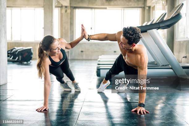 happy sporty couple giving high five to each other while doing push up or side plank exercise together in gym. - athleticism stockfoto's en -beelden