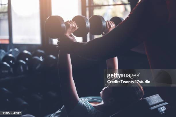young asian woman weightlifting with dumbbells in gym with fitness instructor - instructor de acondicionamiento físico fotografías e imágenes de stock