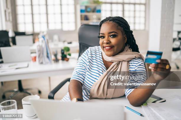 sonriendo afro mujer usando tarjeta de crédito y portátil en casa - chubby credit fotografías e imágenes de stock