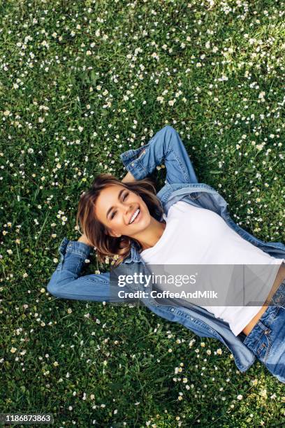 high angle view of smiling young woman lying down on grass - lying on grass stock-fotos und bilder