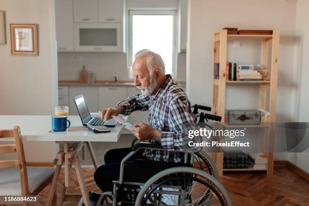disabled senior man in a wheelchair working from home - disability insurance stock pictures, royalty-free photos & images
