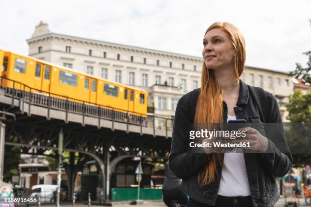 portrait of redheaded young woman with smartphone in the city, berlin, germany - kreuzberg - fotografias e filmes do acervo