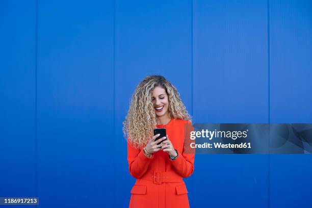 portrait of young woman wearing red dress using cell phone in front of blue background - bright blue background stock pictures, royalty-free photos & images