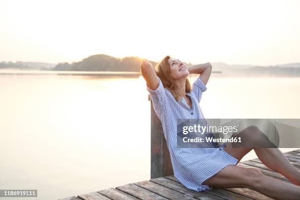 happy mature woman sitting on jetty at a lake at sunrise - holzsteg stock-fotos und bilder