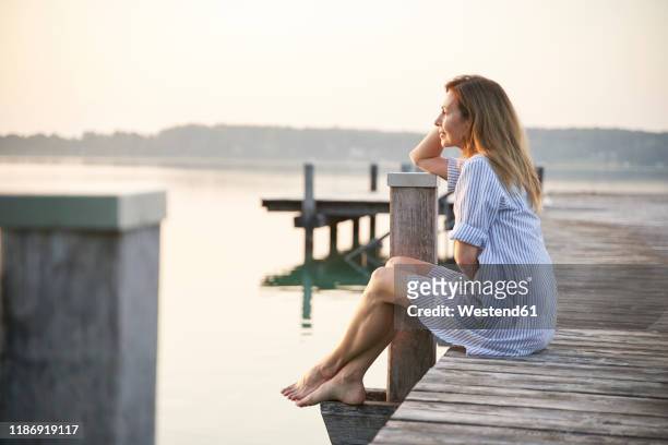 mature woman sitting on jetty at a lake at sunrise - boardwalk stockfoto's en -beelden