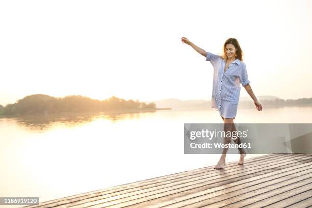 mature woman balancing on jetty at a lake at sunrise - mature woman beauty arm stockfoto's en -beelden