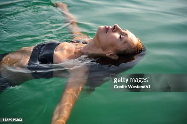 mature woman floating in a lake with closed eyes - swimming stock-fotos und bilder