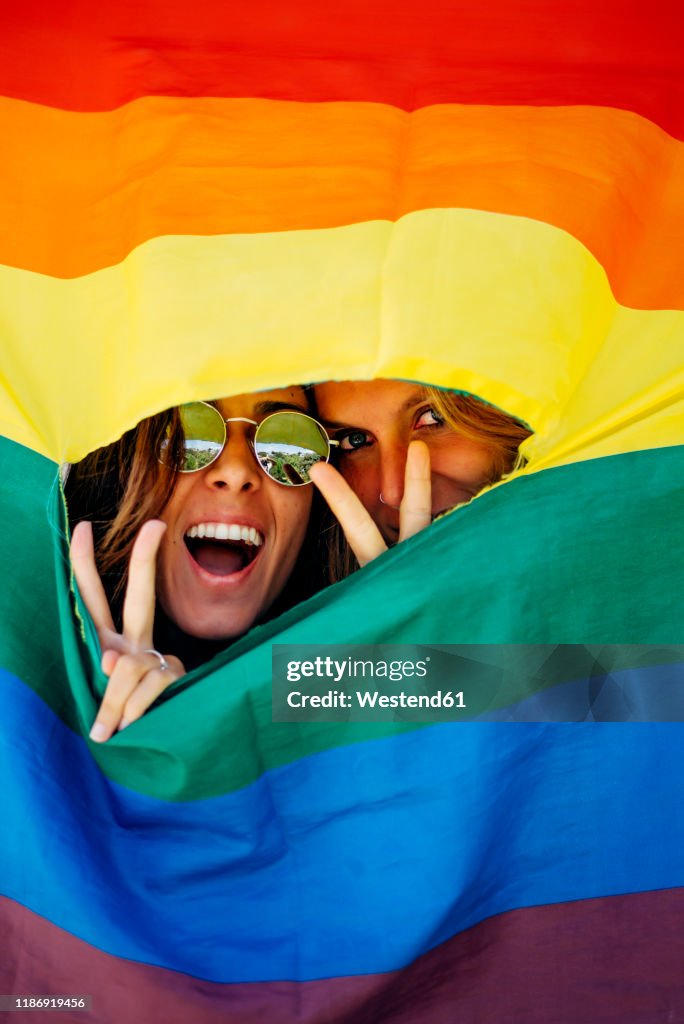 Two women looking through a crack in a rainbow flag
