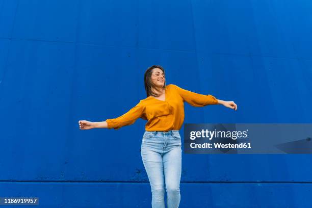 young dancing woman in front of a blue wall - woman wearing white jeans stock-fotos und bilder