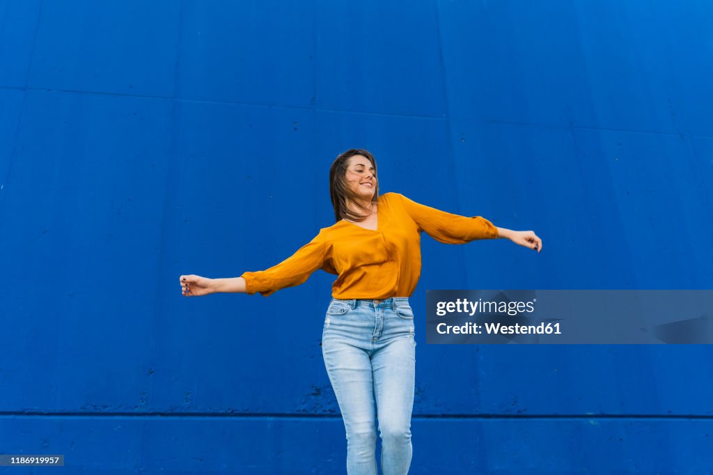 Young dancing woman in front of a blue wall