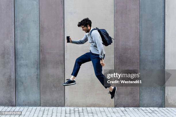 happy man holding cell phone jumping in front of a wall - people in air stock pictures, royalty-free photos & images