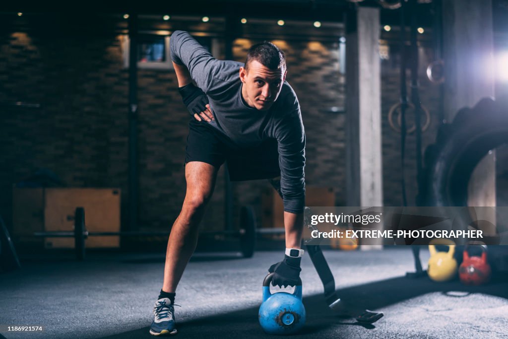 Homem atlético incapacitado novo com uma prótese do pé que faz um exercício do kettlebell em uma ginástica do ajuste transversal