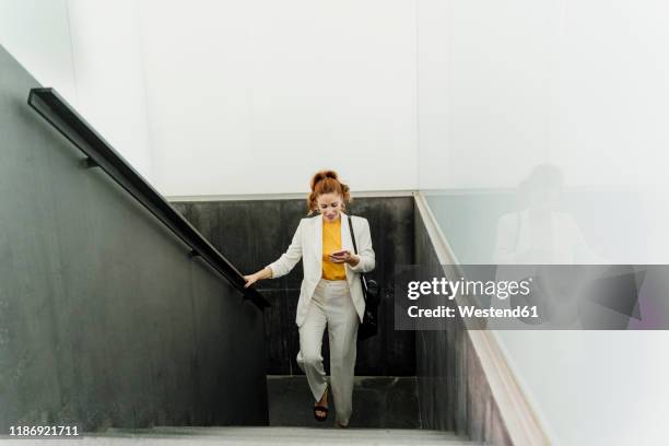 businesswoman in white pant suit, ascending stairs, using smartphone - steps and staircases bildbanksfoton och bilder