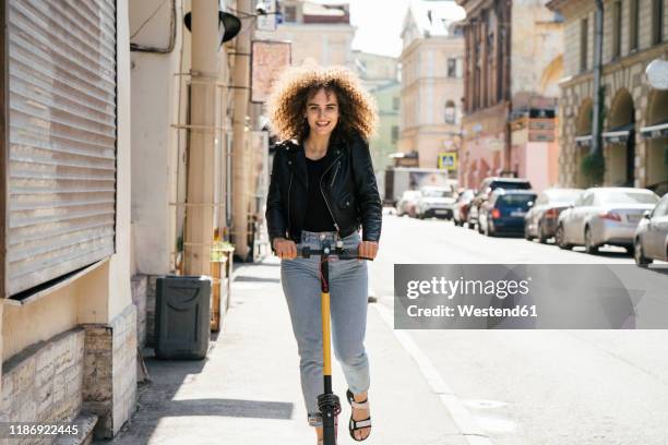 portrait of smiling teenage girl riding scooter on pavement - girl riding scooter stock pictures, royalty-free photos & images