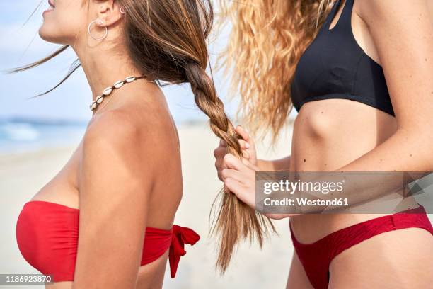 young woman braidng the hair of her friend on the beach - natte photos et images de collection