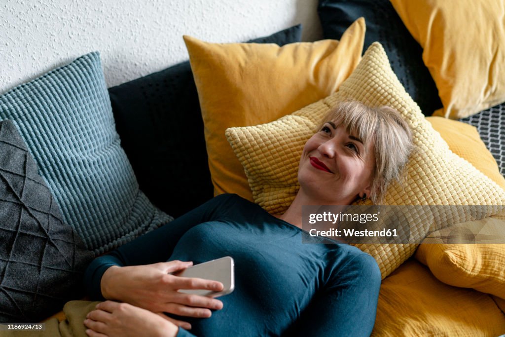Portrait of happy woman lying on the couch with smartphone