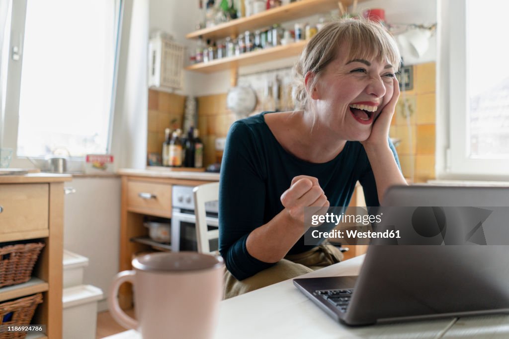 Portrait of woman sitting in the kitchen with laptop crying for joy