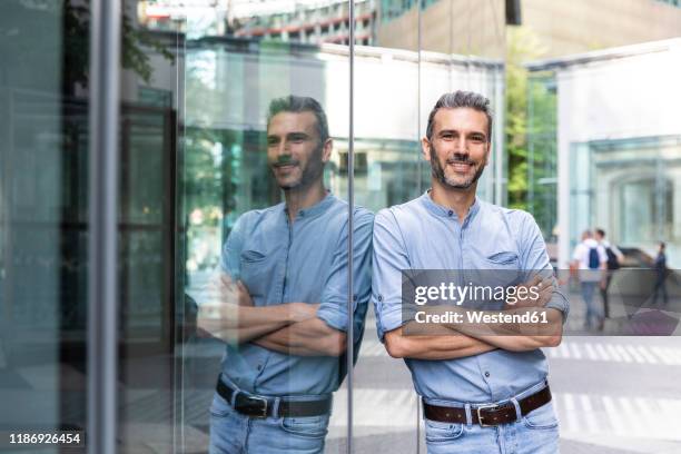 smiling businessman with reflection on a glass facade, berlin, germany - man reflection foto e immagini stock