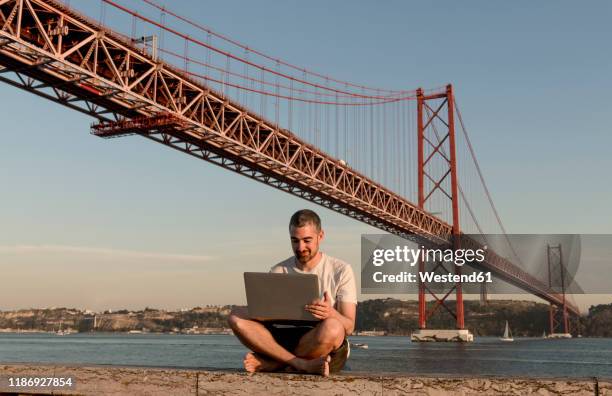 man using laptop at 25th of april bridge in lisbon, portugal - puente 25 de abril fotografías e imágenes de stock