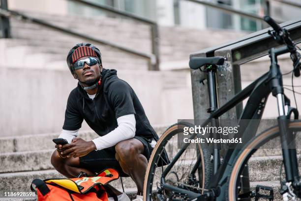 stylish young man with bicycle, smartphone and messenger bag in the city - bicycle courier stock pictures, royalty-free photos & images