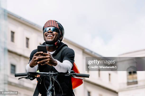 happy stylish young man with bicycle, smartphone and messenger bag in the city - fahrrad kurier stock-fotos und bilder