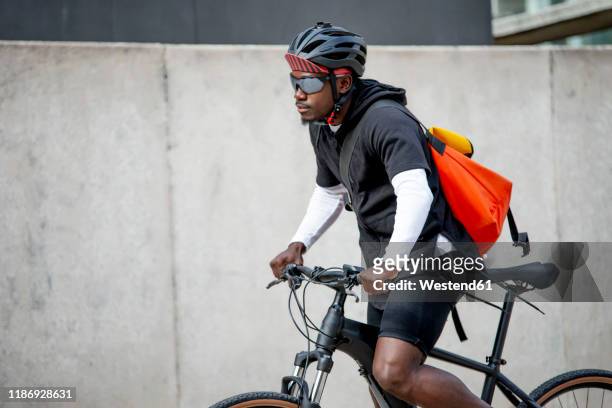 stylish young man with messenger bag riding bicycle in the city - bicycle courier stock pictures, royalty-free photos & images