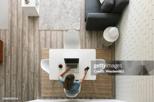 woman sitting at table in modern loft using laptop and smartphone, top view - empty office one person stock pictures, royalty-free photos & images