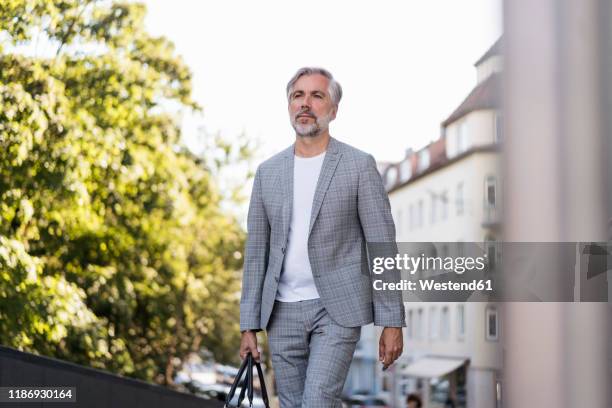 fashionable mature businessman with travelling bag on the go in the city - geblokt pak stockfoto's en -beelden