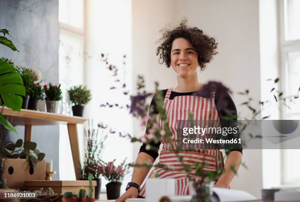 portrait of smiling young woman in a small shop with plants - florist stock-fotos und bilder