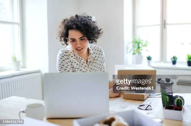 smiling young woman preparing a package at desk - laptop work search stockfoto's en -beelden