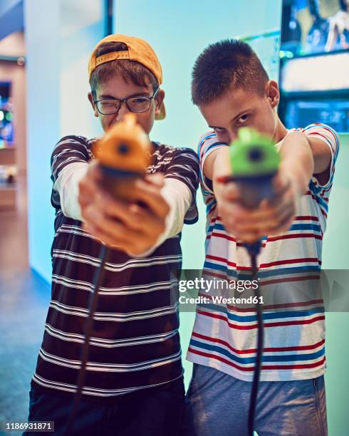 portrait of teenage friends shooting with pistols in an amusement arcade - pistola de juguete fotografías e imágenes de stock