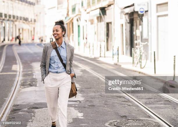 smiling young woman with wireless earphones in the city on the go, lissabon, portugal - in ear headphones photos et images de collection