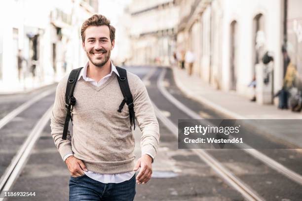 portrait of smiling young man with backpack in the city on the go, lissabon, portugal - mann pullover stock-fotos und bilder