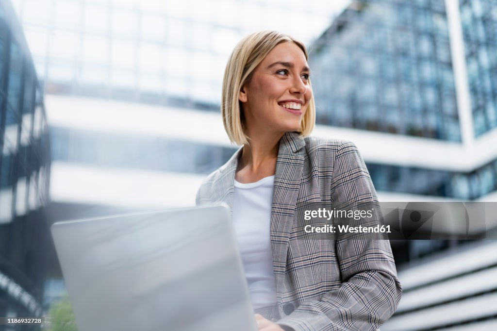 Smiling young businesswoman using laptop in the city