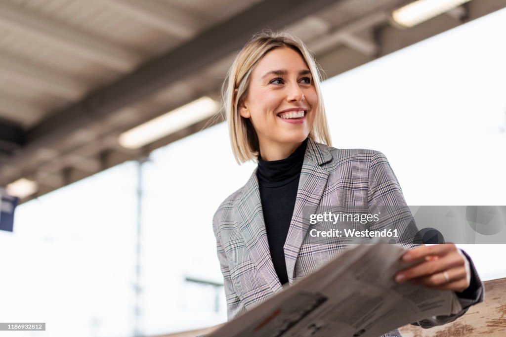 Smiling young businesswoman with newspaper at the train station