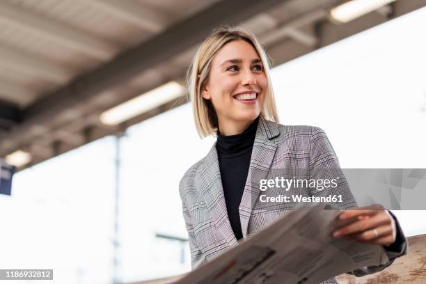 smiling young businesswoman with newspaper at the train station - woman relaxed portrait sitting stock-fotos und bilder