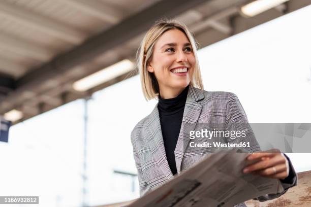 smiling young businesswoman with newspaper at the train station - blazer 個照片及圖片檔