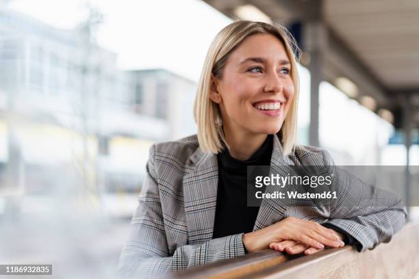 happy young businesswoman at the train station looking around - grijze blazer stockfoto's en -beelden