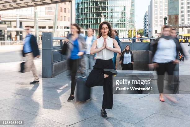 young businesswoman practising yoga in the city at rush hour, berlin, germany - hauptverkehrszeit stock-fotos und bilder
