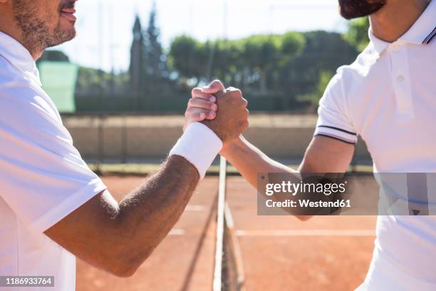 side view of two tennis players with rackets shaking hands and smiling before tennis match - loyalty foto e immagini stock