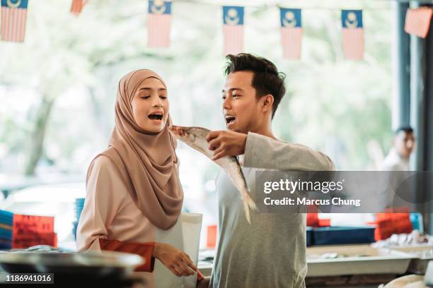 asian malay couple taking a fish and acting like want to eat, playing in front of fish stall - malay couple stock pictures, royalty-free photos & images